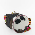 Detalle de la base del bolso de estampado de vaca y cuero fucsia con correa Wayuu de colores vibrantes.