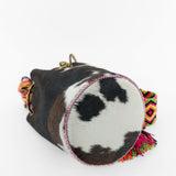 Detalle de la base del bolso de estampado de vaca y cuero fucsia con correa Wayuu de colores vibrantes.