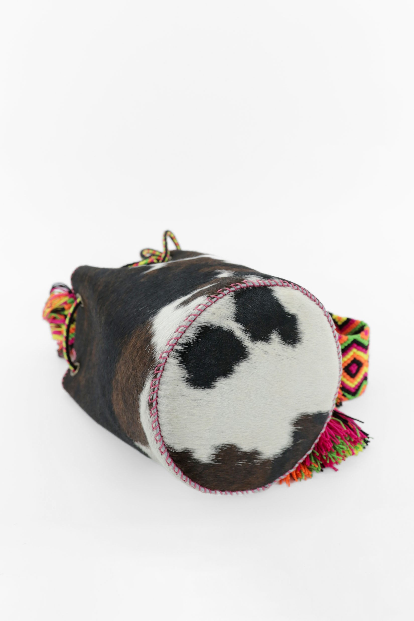 Detalle de la base del bolso de estampado de vaca y cuero fucsia con correa Wayuu de colores vibrantes.